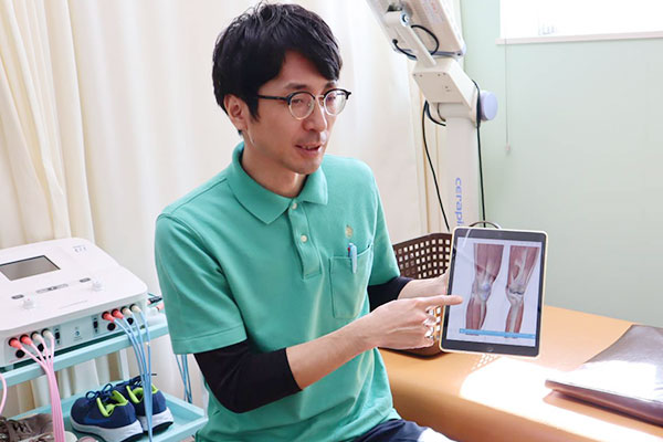 タブレットを使って膝の状態や体の使い方について分かりやすく説明している施術風景